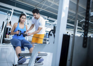 Gym woman with personal trainer on weight machines